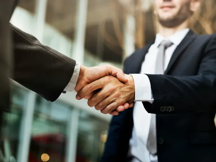 Close-up of two businessmen shaking hands confidently in bright modern office, symbolizing partnership success
